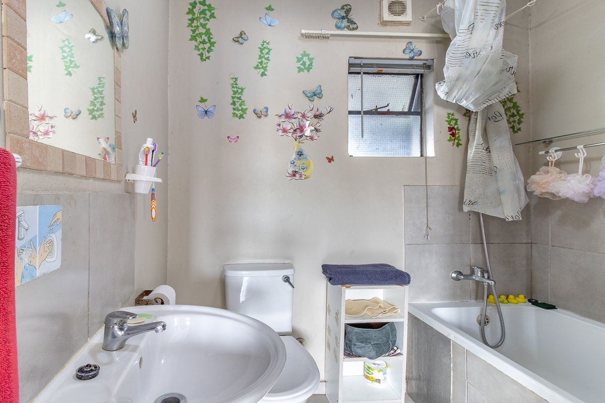 A functional bathroom featuring a pedestal basin, toilet, and bathtub with a tiled splashback and an integrated extractor fan.
