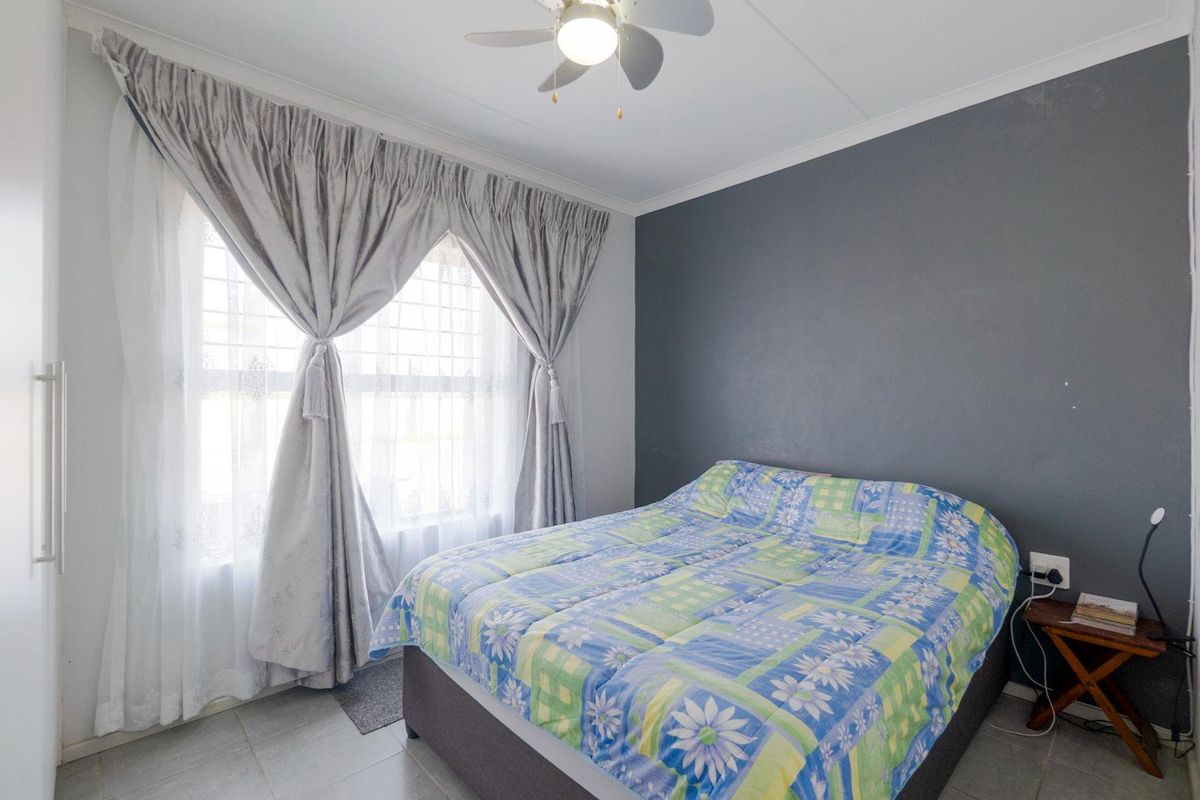 A bedroom featuring tiled flooring, a ceiling fan, and a dark accent wall, providing a functional and comfortable sleeping space.