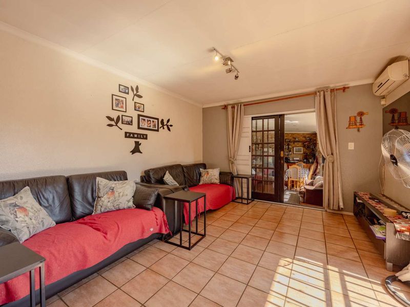 A comfortable living room featuring tiled flooring, a wall-mounted air conditioning unit, and glass-paned french doors leading to an adjacent space.