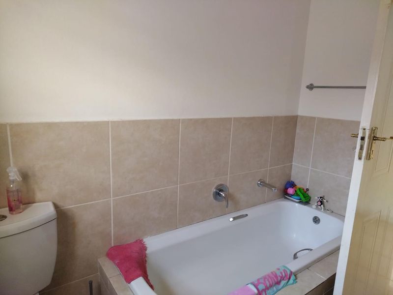 A functional bathroom featuring a built-in bathtub with wall-mounted fixtures and neutral wall tiling.
