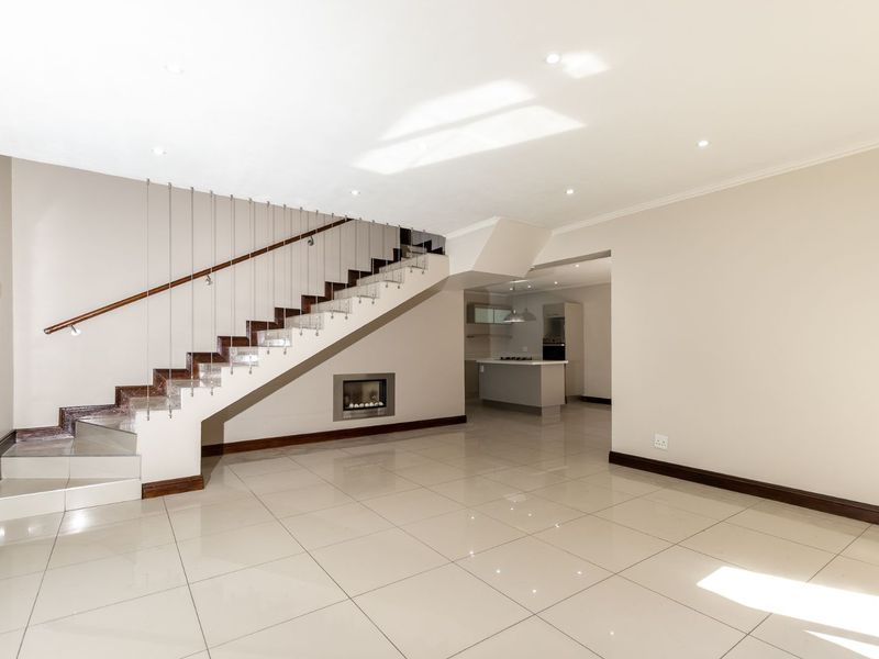 Spacious open-plan living area featuring polished tile flooring, a modern staircase with cable railing, a built-in fireplace, and an adjoining kitchen space.