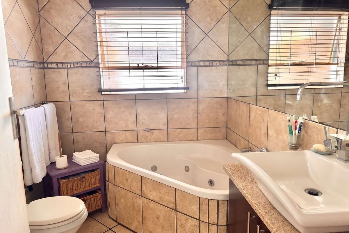 A functional bathroom featuring a corner spa bath, vessel sink vanity, and neutral tiled finishes throughout.