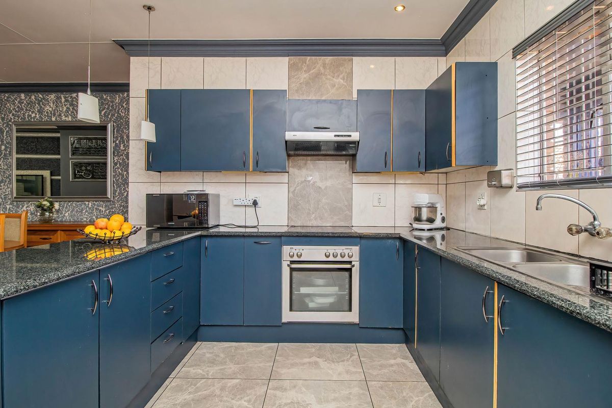 A well-maintained kitchen featuring blue cabinetry, granite countertops, a built-in oven with extractor fan, and tiled finishes throughout.