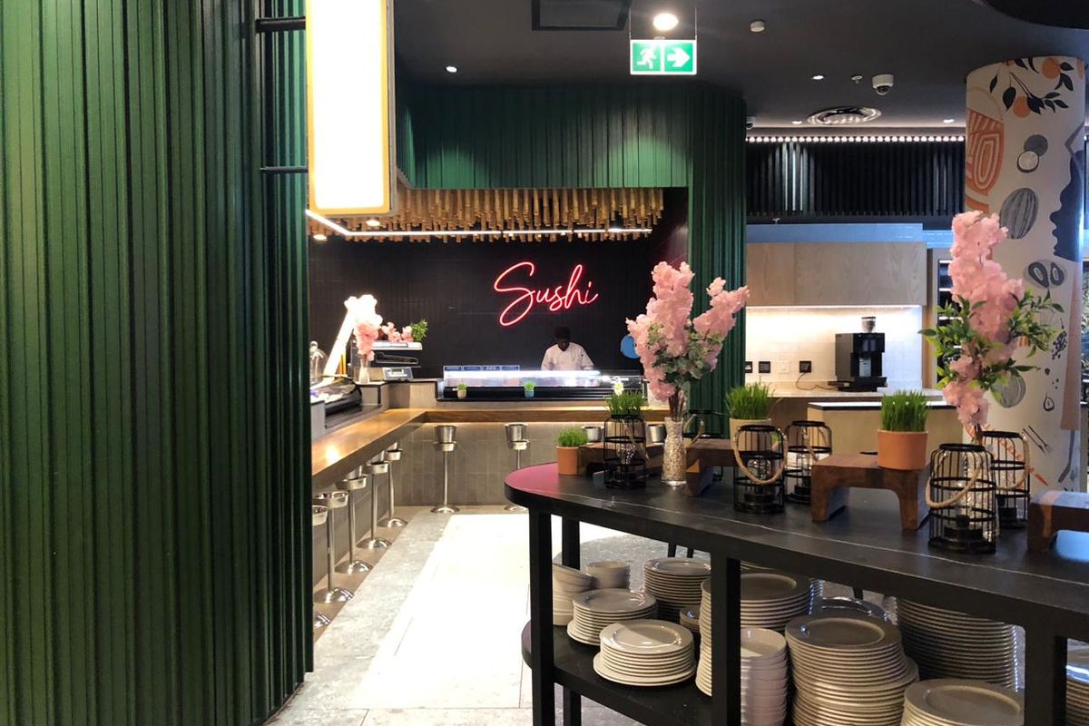 A modern, well-maintained sushi preparation area featuring a built-in counter, decorative green wall paneling, and professional commercial kitchen lighting.