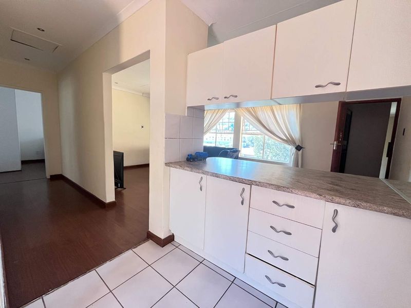 A functional kitchen area featuring white built-in cabinetry, laminate countertops, and tiled flooring, offering a clean and neutral space for potential updates.