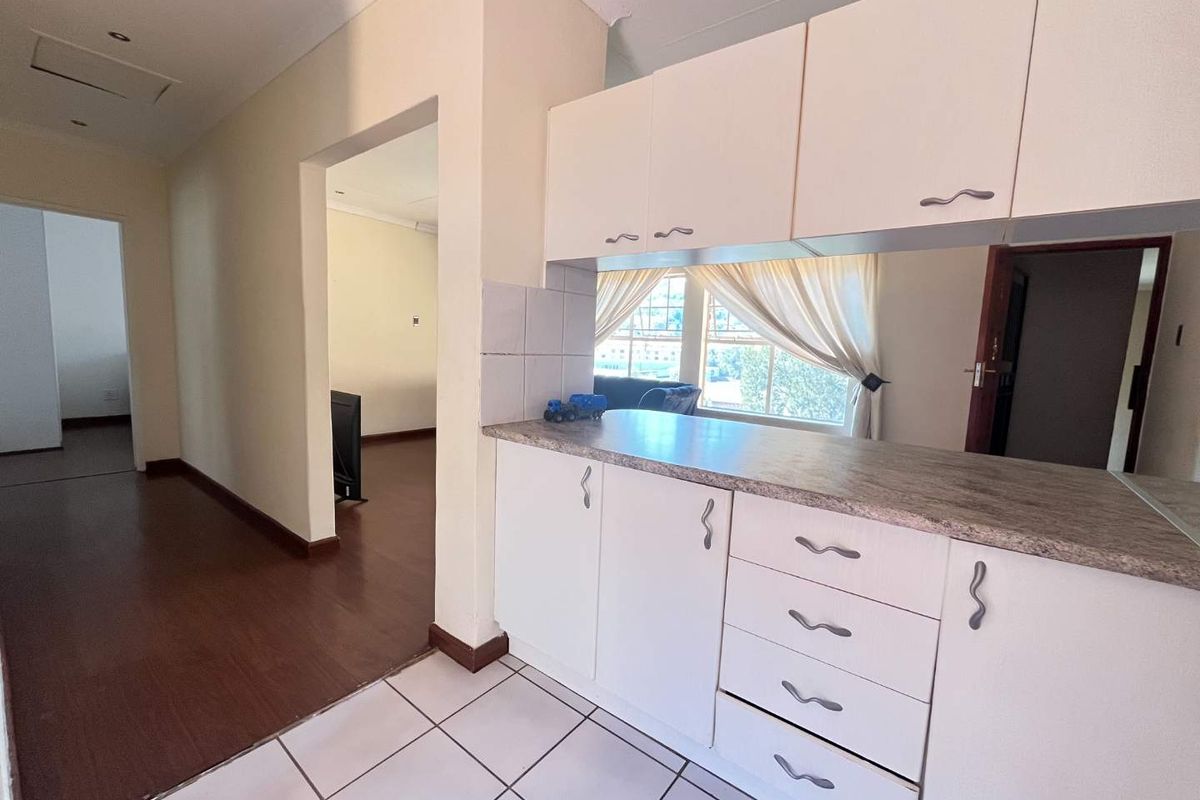 A functional kitchen area featuring white built-in cabinetry, laminate countertops, and tiled flooring, offering a clean and neutral space for potential updates.
