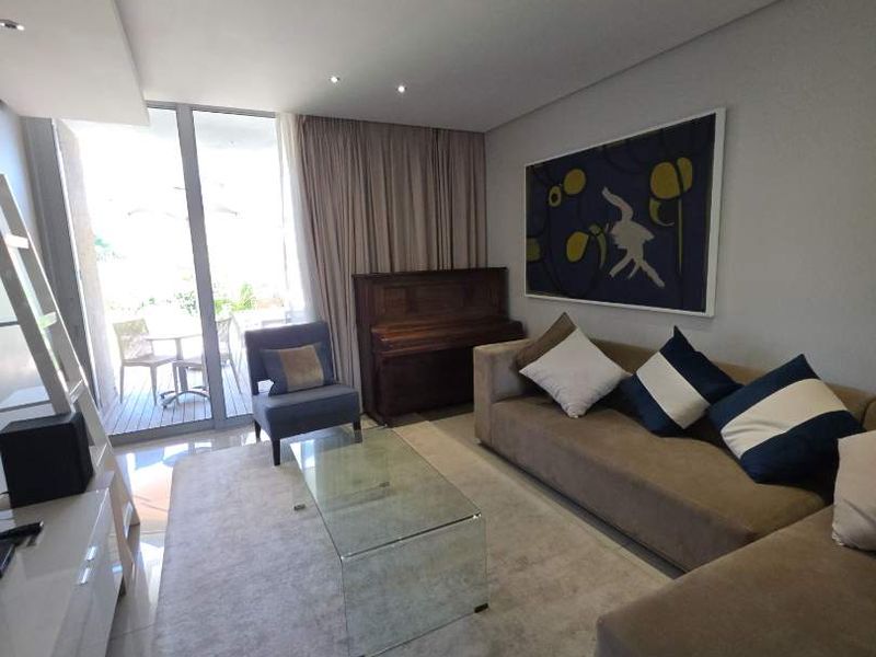 A bright and modern living room featuring tiled floors, recessed lighting, and large sliding glass doors providing access to an outdoor balcony area.