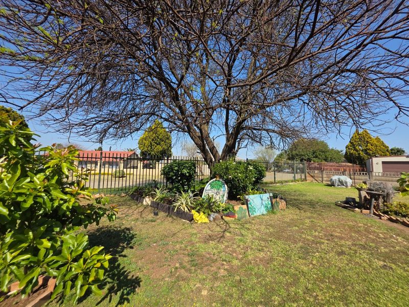 A spacious residential garden featuring a large mature tree, established garden beds, and secure metal perimeter fencing.