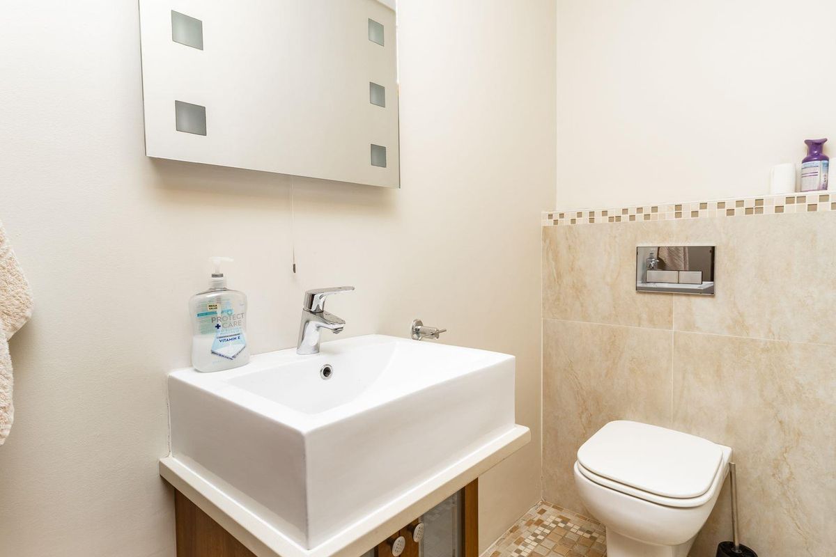 A compact bathroom featuring a wall-mounted toilet with a concealed cistern, a modern vessel sink vanity, and a wall-mounted mirror.