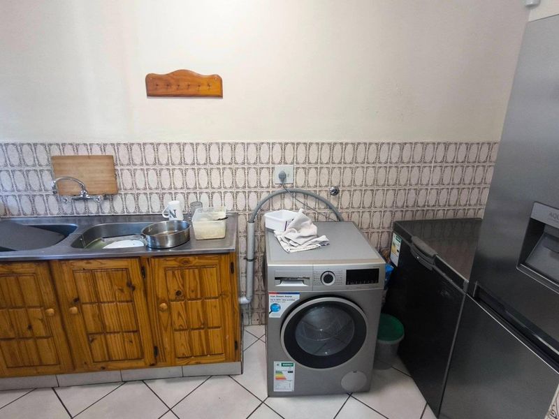 A functional laundry area featuring a stainless steel sink, wooden cabinetry, and tiled backsplash, providing essential utility space for the home.