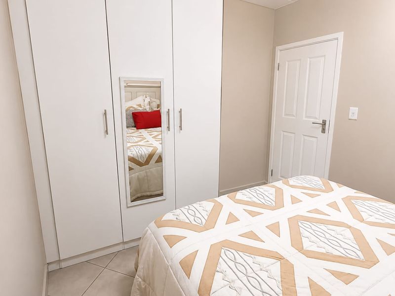 A well-maintained bedroom featuring built-in wardrobes with a mirrored panel, neutral wall tones, and tiled flooring.