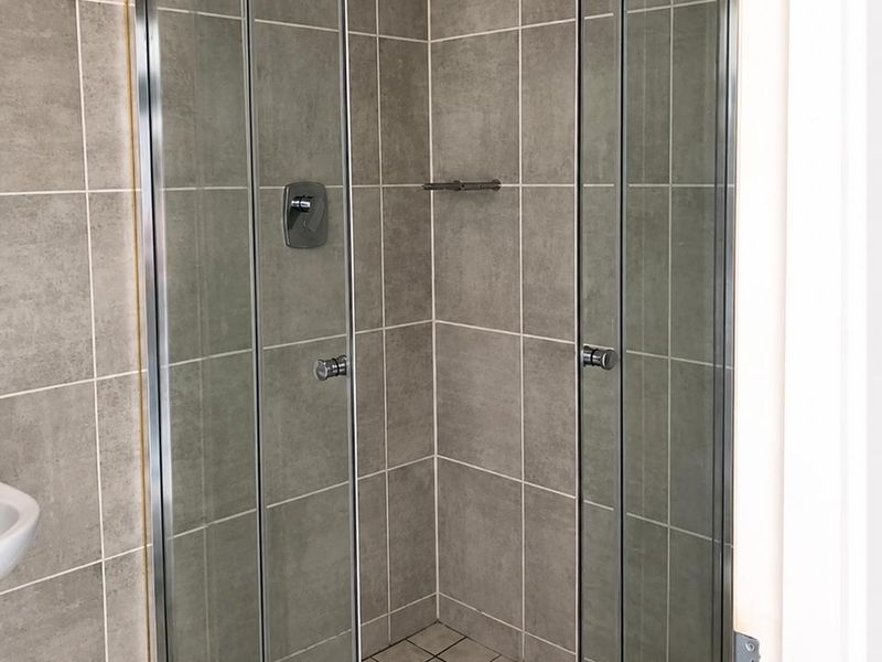 A clean bathroom shower enclosure featuring grey wall tiles, a glass door, and a tiled floor base.