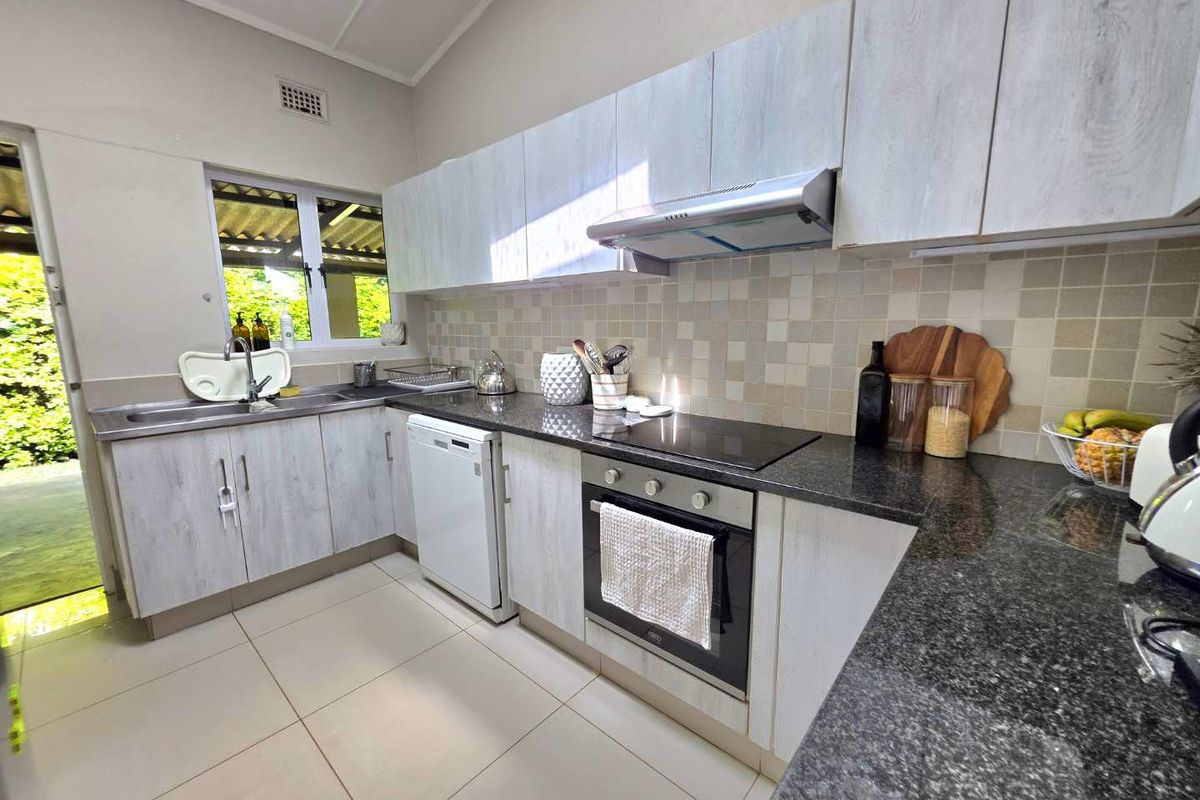 A functional kitchen featuring light wood-grain cabinetry, dark granite countertops, a built-in oven, extractor fan, and tiled flooring with direct access to the outdoors.