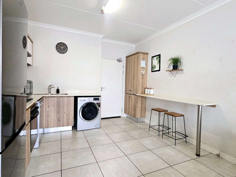 A functional kitchen featuring light wood-finish cabinetry, tiled flooring, a built-in breakfast bar, and integrated space for laundry appliances.