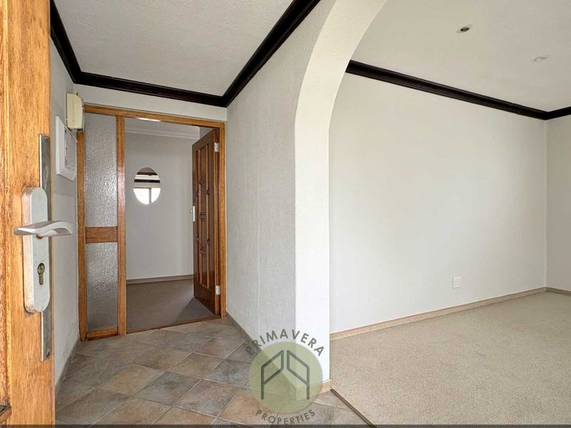 A bright entrance hall featuring tiled flooring, an arched transition to the living area, and a timber-framed door leading to an adjacent room.