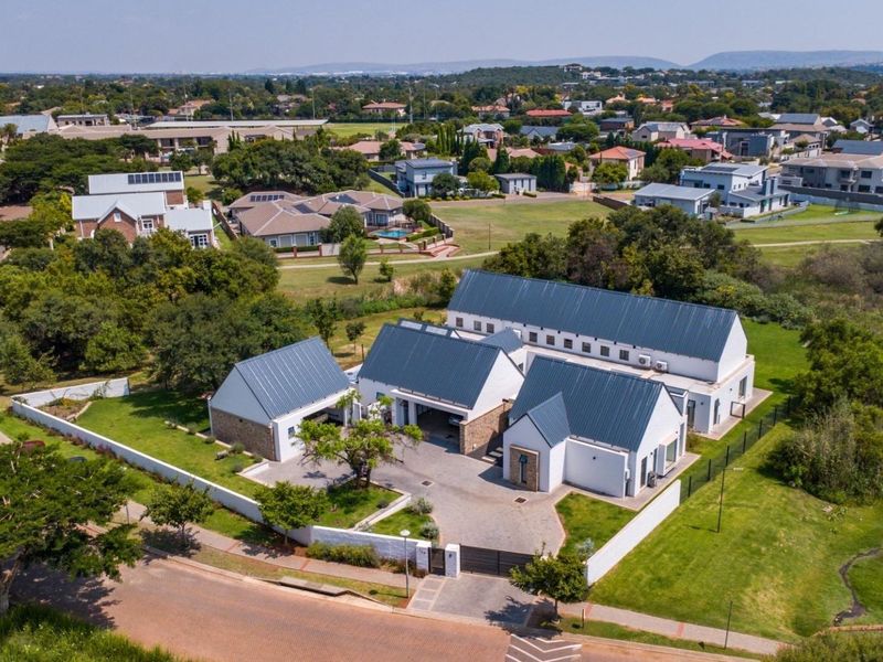 Aerial view of a modern residential property featuring multiple structures with metal roofing, a paved driveway, and a secure perimeter wall in a suburban estate.