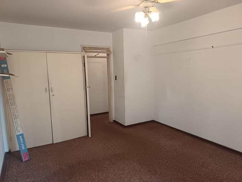 An empty bedroom featuring built-in cupboards, a ceiling fan, and carpeted flooring, offering a blank canvas for renovation or restyling.