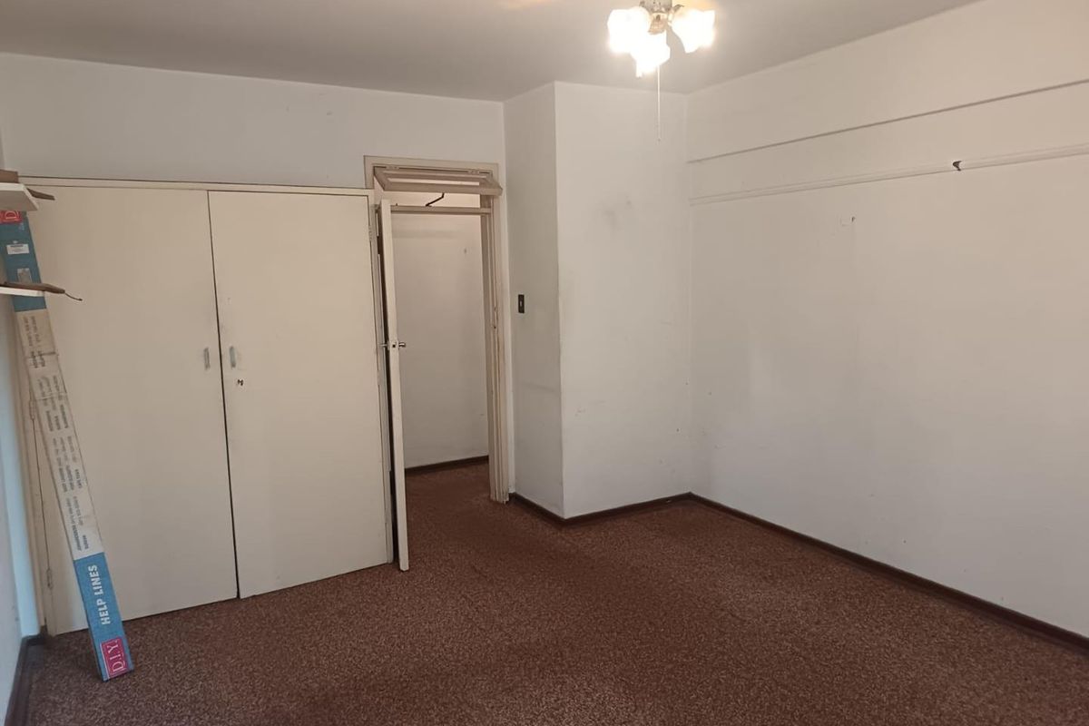 An empty bedroom featuring built-in cupboards, a ceiling fan, and carpeted flooring, offering a blank canvas for renovation or restyling.