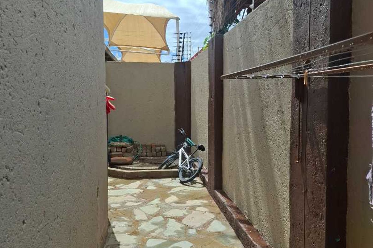 A narrow side passage featuring stone paving, boundary walls with integrated electric fencing, and a wall-mounted drying rack.