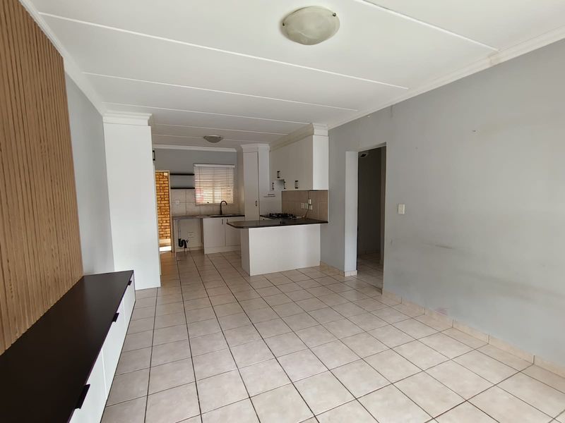 An open-plan living and kitchen area featuring tiled flooring, a functional kitchen peninsula with a hob, and a decorative slatted wood wall feature.