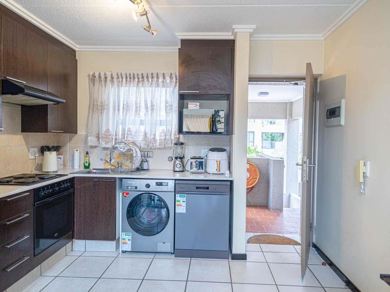 A functional kitchen featuring dark wood cabinetry, tiled flooring, built-in oven and hob, and direct access to an outdoor area.