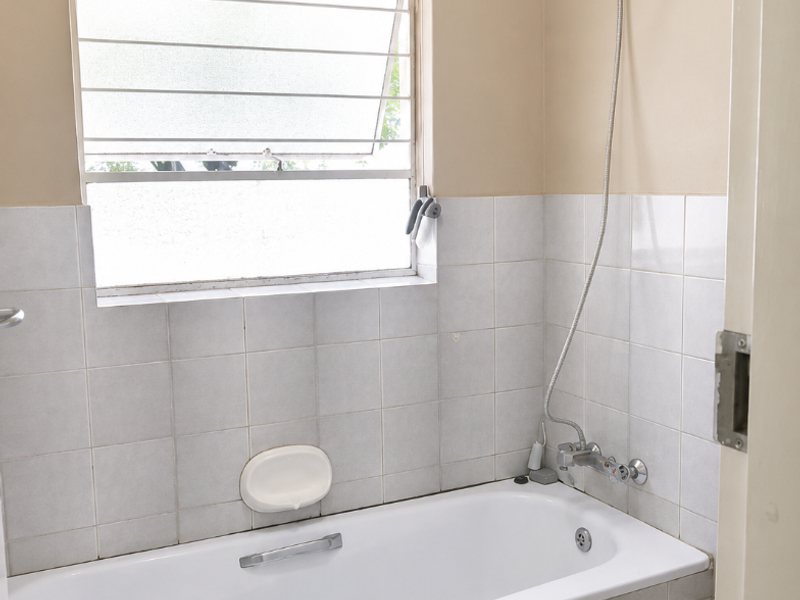 A functional bathroom featuring a bathtub with a handheld shower attachment, tiled splashback, and a louver window for ventilation.