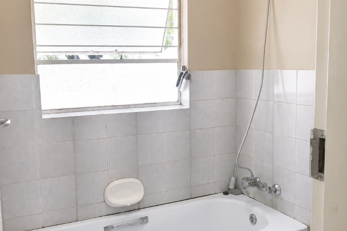 A functional bathroom featuring a bathtub with a handheld shower attachment, tiled splashback, and a louver window for ventilation.