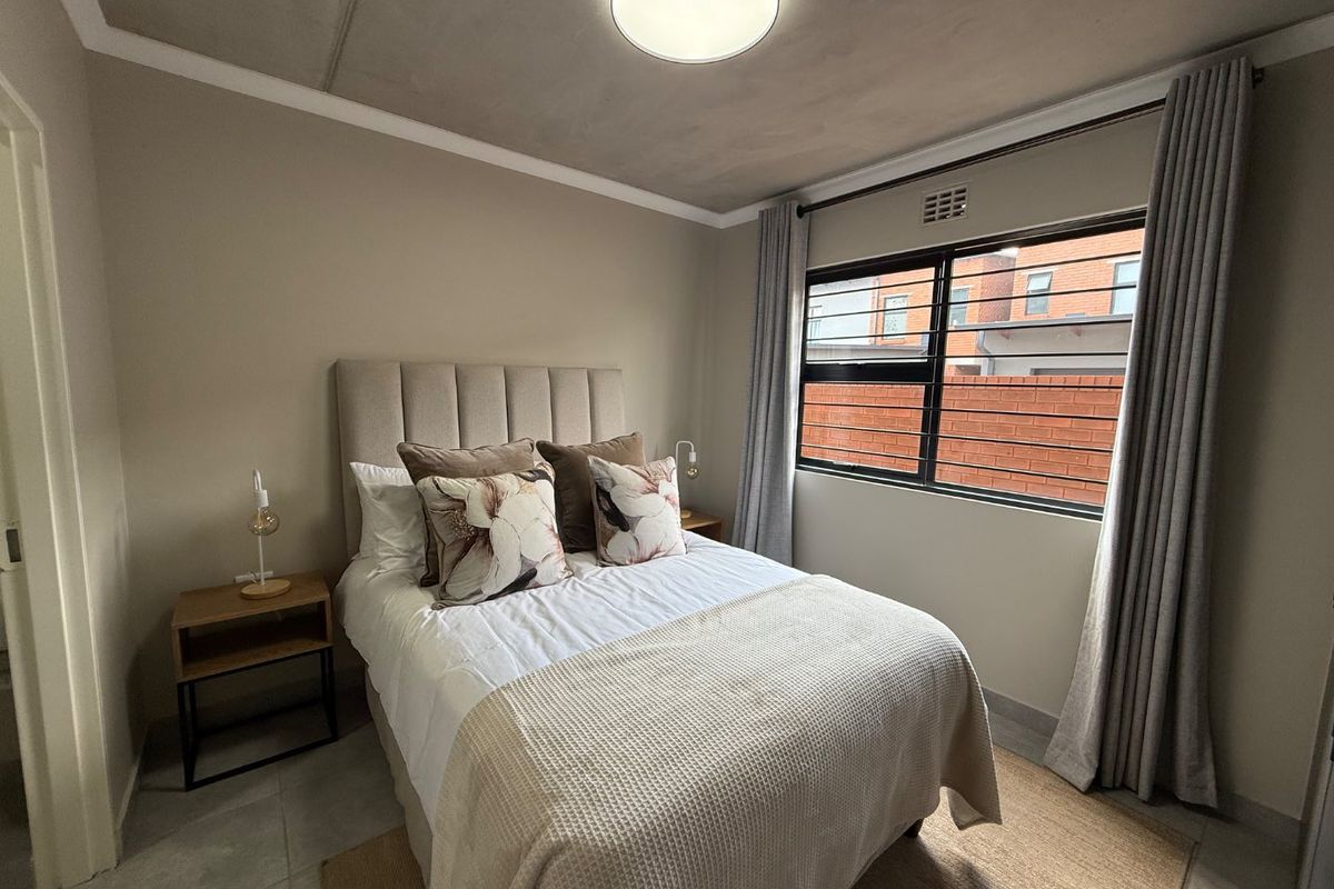 A well-maintained bedroom featuring tiled flooring, a window with security bars, and neutral wall finishes.