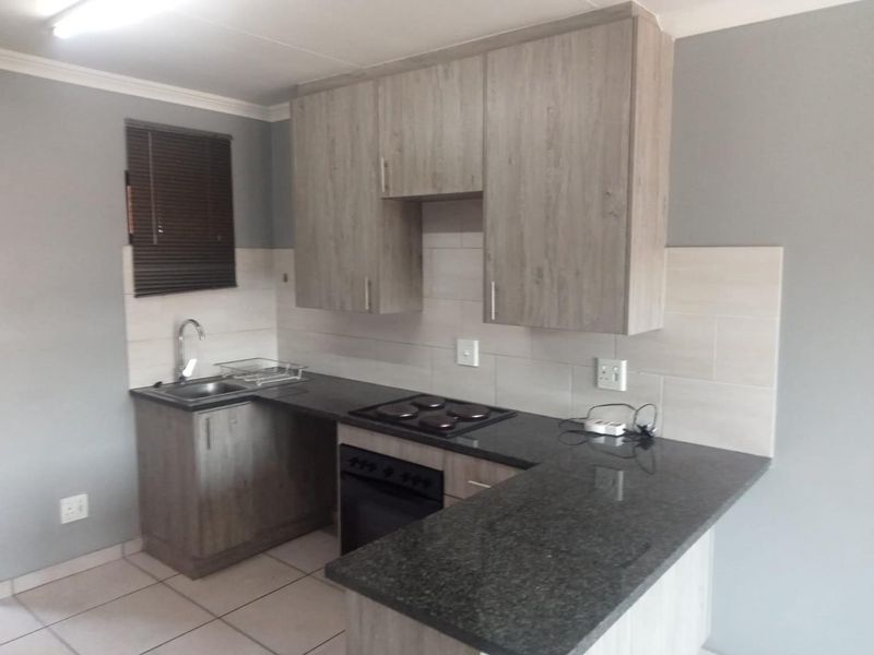 A compact, modern kitchen featuring light wood-grain cabinetry, dark granite countertops, a built-in oven and hob, and neutral tiled finishes.