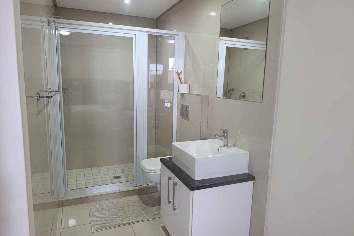 Modern bathroom featuring a glass shower enclosure, a contemporary vessel sink with vanity cabinet, and a wall-mounted toilet with neutral wall and floor tiling.