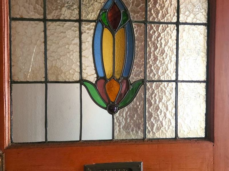 A close-up view of a classic timber entrance door featuring decorative stained glass paneling and a built-in metal letter slot.