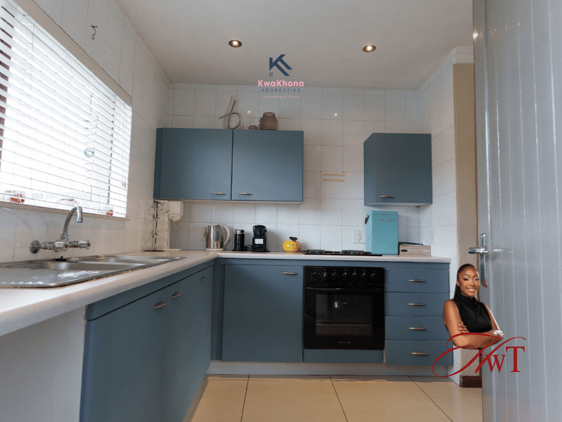 A functional kitchen featuring blue cabinetry, a built-in oven, hob, and stainless steel sink with tiled splashbacks and recessed lighting.