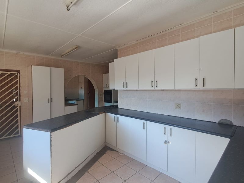 A vacant kitchen featuring white built-in cabinetry, dark countertops, and tiled flooring, offering a functional layout ready for modern updates and renovation.