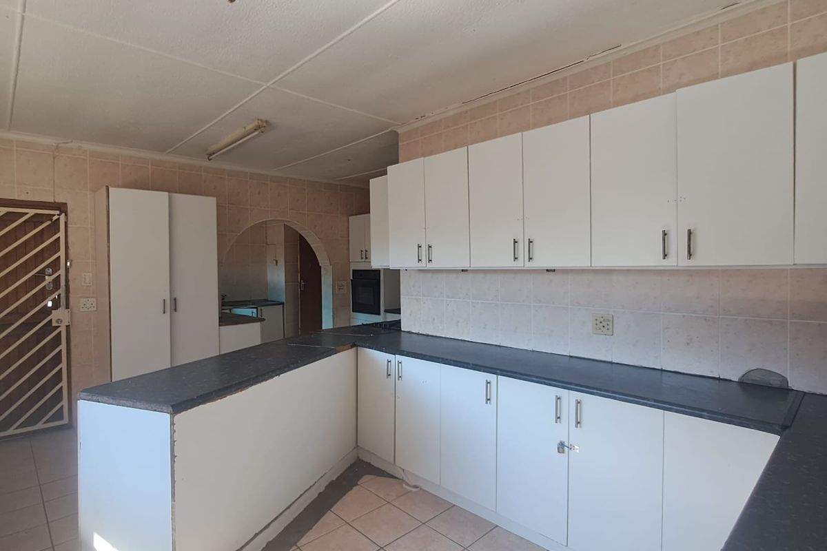 A vacant kitchen featuring white built-in cabinetry, dark countertops, and tiled flooring, offering a functional layout ready for modern updates and renovation.