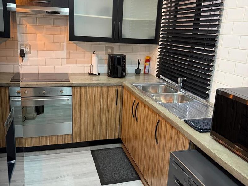 A modern, well-maintained kitchen featuring wood-grain cabinetry, subway tile backsplash, integrated oven and hob, and a functional double sink setup.