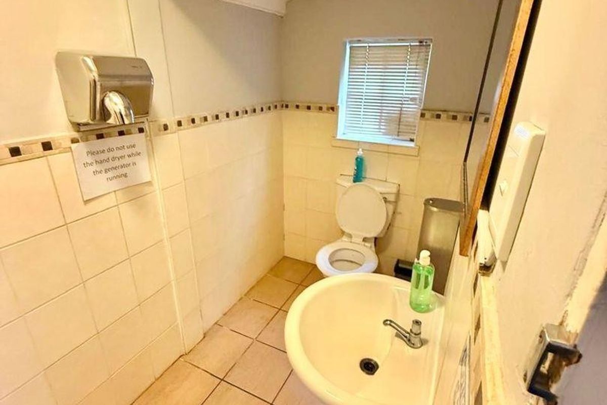 A functional restroom featuring a pedestal sink, toilet, and wall-mounted hand dryer with tiled walls and flooring.