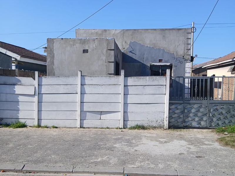 Front view of a residential property featuring an unpainted cement facade, a precast concrete boundary wall, and a metal entrance gate.
