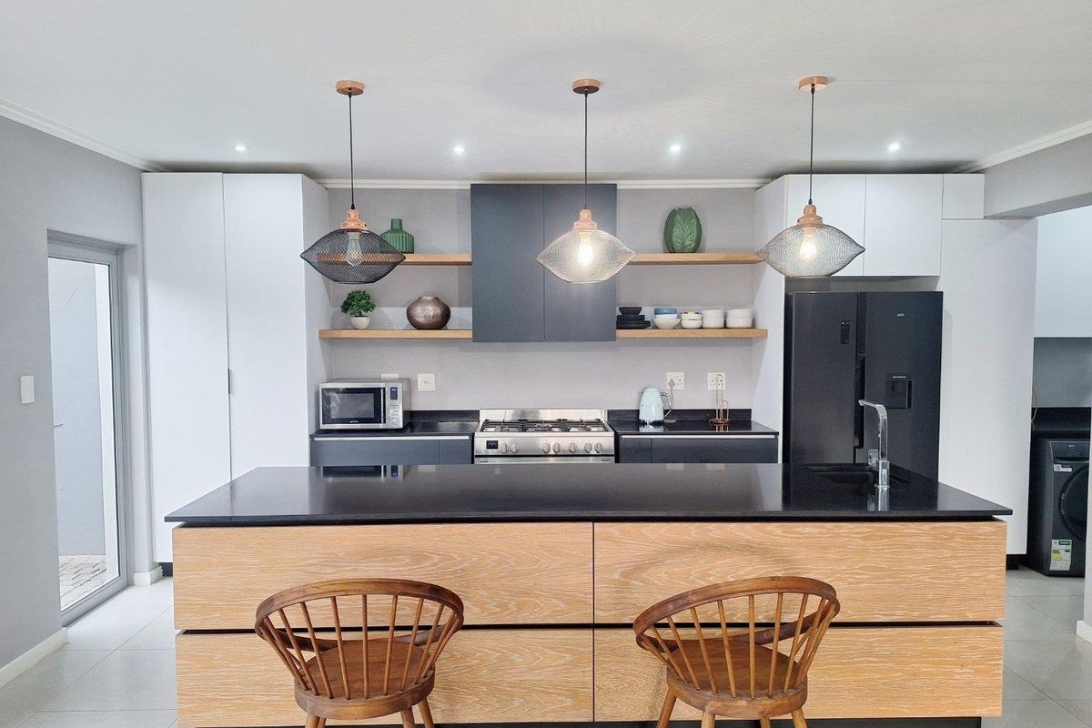 Modern kitchen featuring a large wooden island with black countertop, gas hob, extractor fan, and sleek two-tone cabinetry with open shelving.