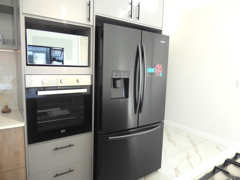 Modern kitchen featuring sleek grey cabinetry, built-in oven and microwave, and elegant marble-look floor tiles.