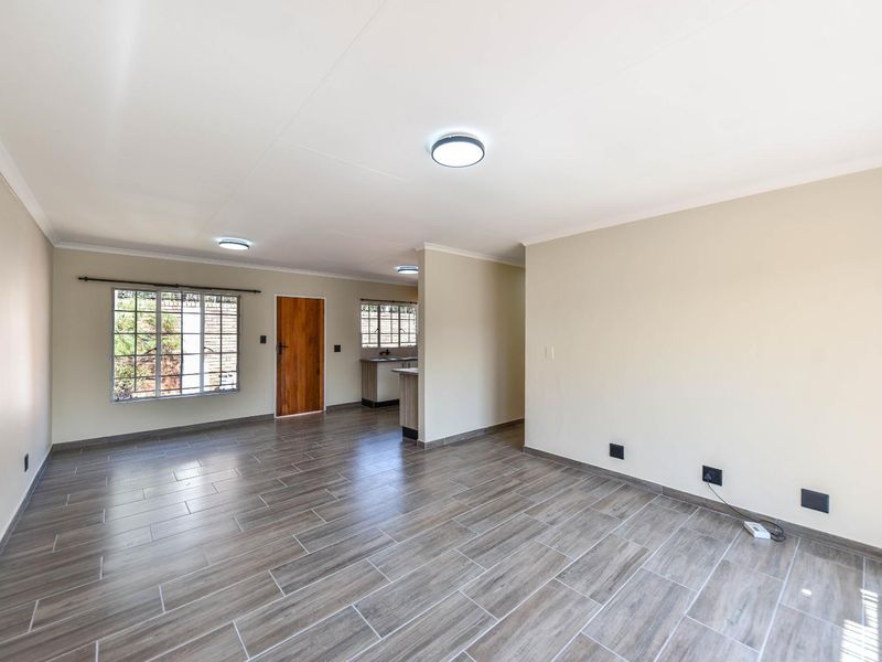Spacious open-plan living area featuring modern wood-look tiled flooring, neutral walls, and direct access to the kitchen and entrance.