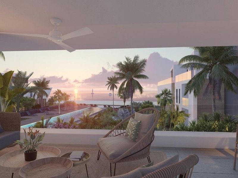 A spacious covered balcony featuring a modern ceiling fan, slatted timber accents, and a glass balustrade overlooking a resort-style pool and ocean view.