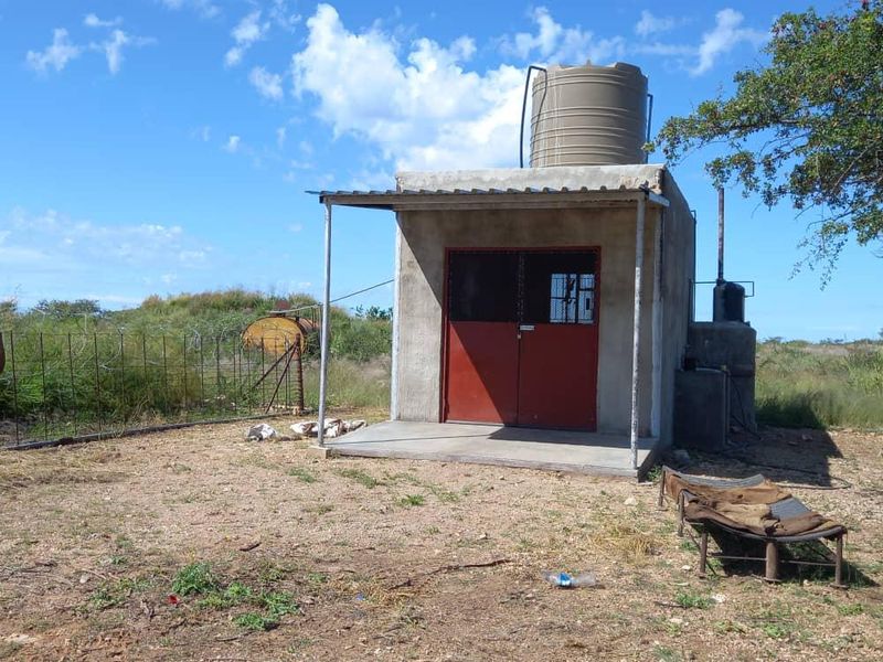 A functional utility outbuilding on the farm property, featuring a concrete structure, metal security door, and an elevated water storage tank.