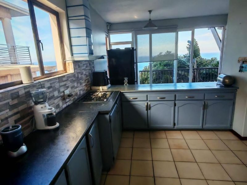A functional kitchen featuring built-in cabinetry, a gas hob, and tiled flooring, offering expansive views through large windows.