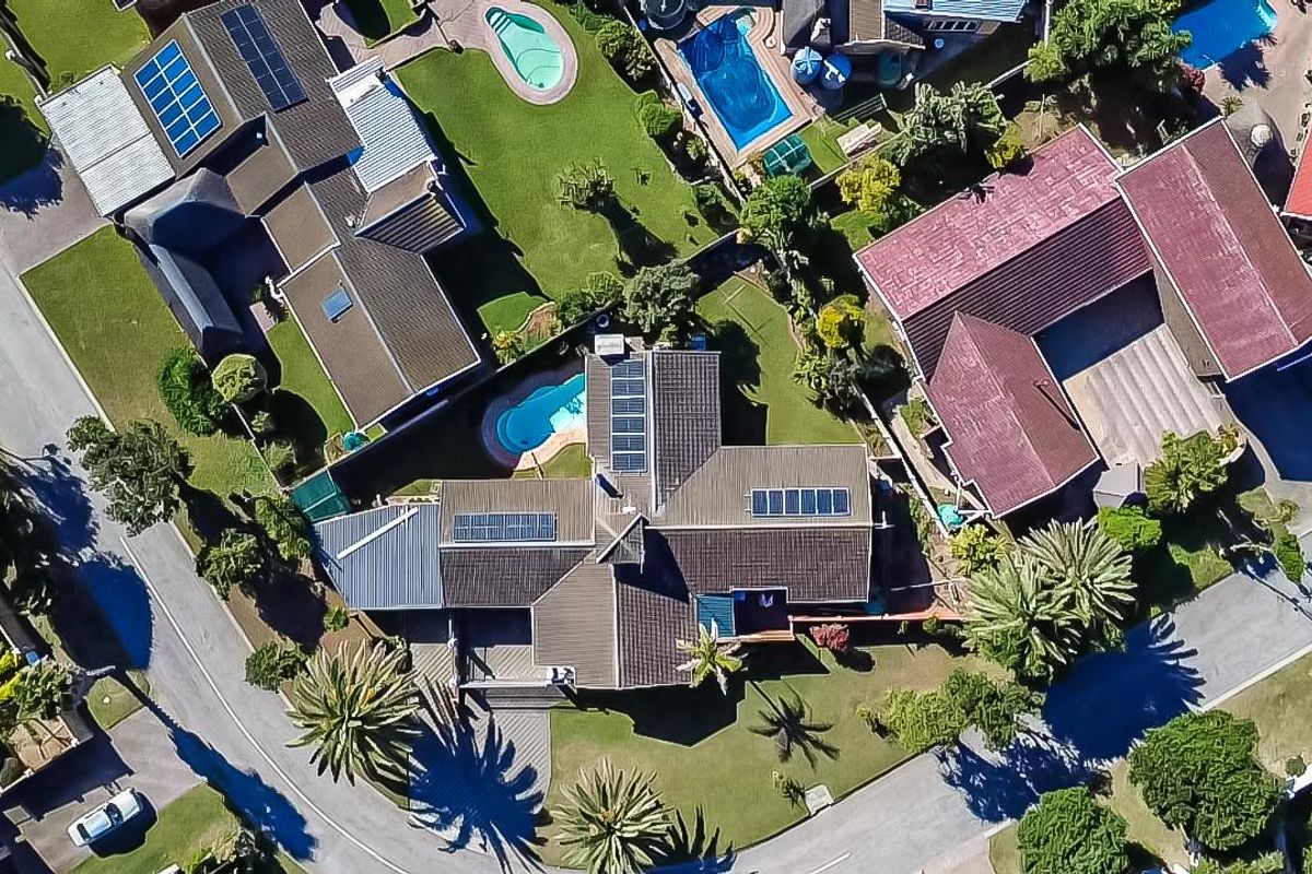Aerial view of a residential property featuring a swimming pool, solar panels, and well-maintained garden areas within a suburban neighborhood.