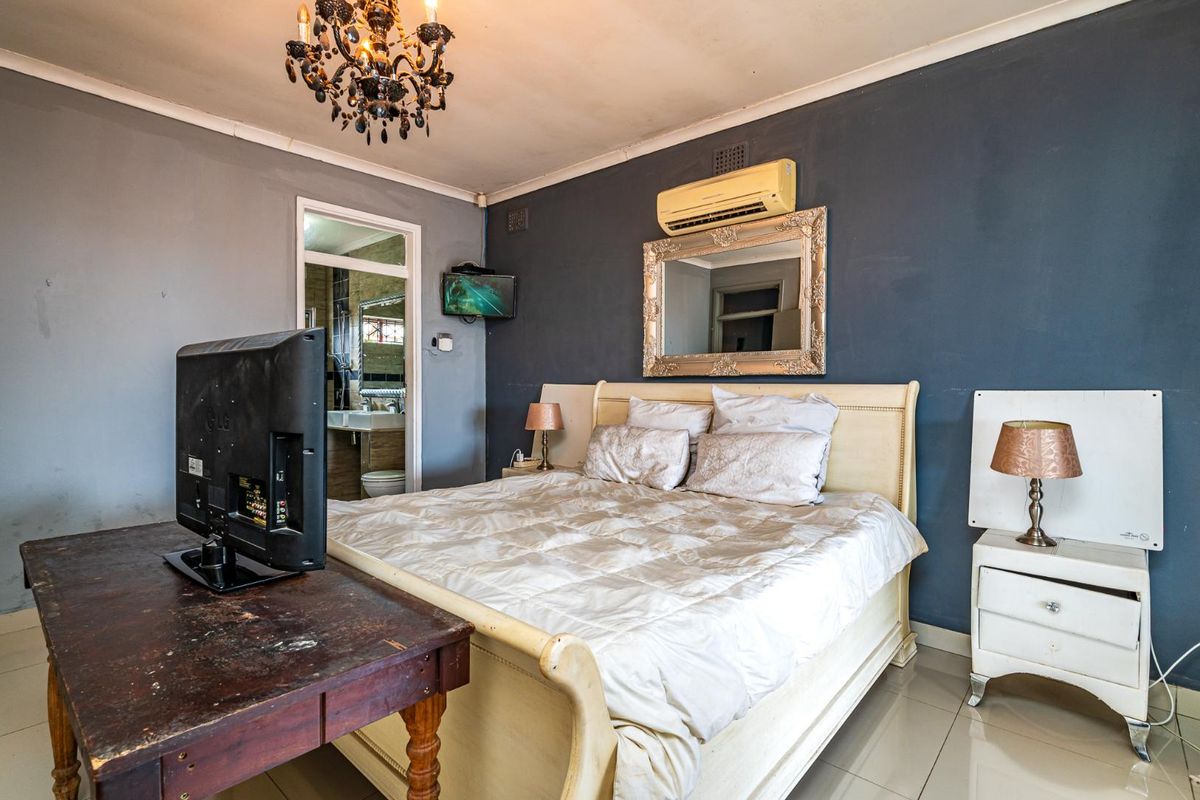 A bedroom featuring tiled flooring, a wall-mounted air conditioning unit, and an en-suite bathroom access.