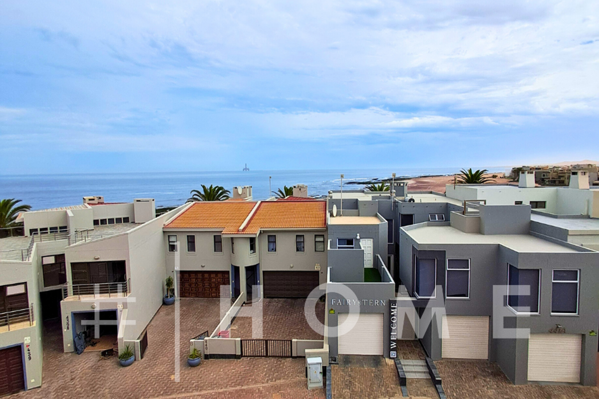 Aerial view of a coastal apartment complex featuring paved driveways, multiple garage units, and modern architectural facades overlooking the ocean.