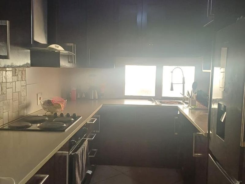 A compact kitchen featuring dark wood cabinetry, a built-in oven, electric hob, and tiled flooring, offering a functional layout for daily meal preparation.