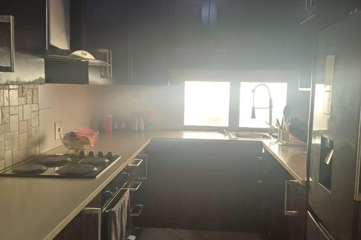 A compact kitchen featuring dark wood cabinetry, a built-in oven, electric hob, and tiled flooring, offering a functional layout for daily meal preparation.