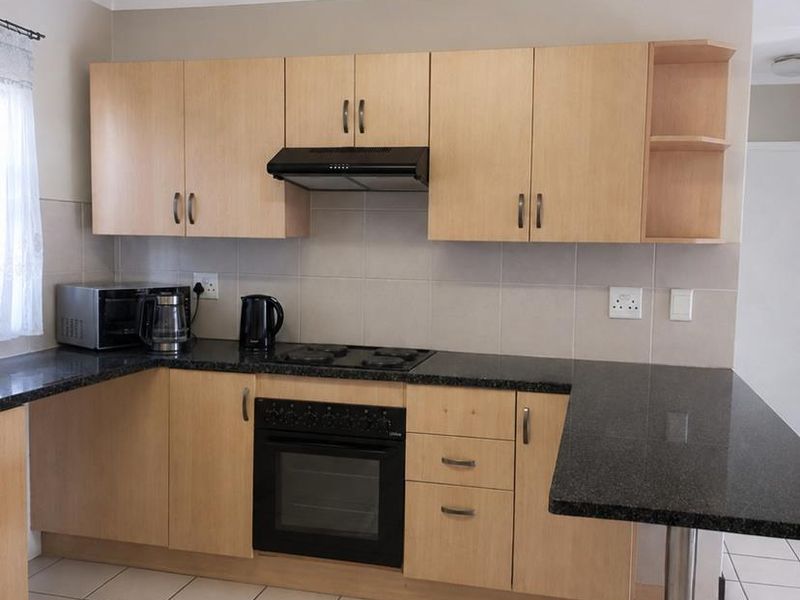A functional kitchen featuring light wood cabinetry, dark granite countertops, a built-in oven with hob, and a breakfast bar extension.