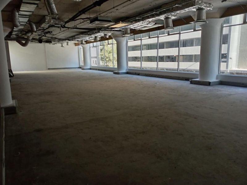 A spacious, open-plan office area featuring exposed industrial ceilings, concrete flooring, and large windows providing ample natural light.